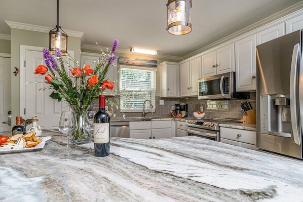 A kitchen with marble countertops, stainless steel appliances, and a vase with flowers on the island.