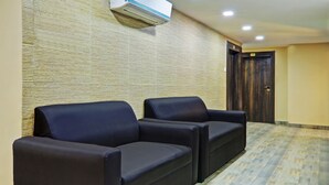 Un área de espera con dos sillones de cuero negro, un pared texturizada, una puerta de madera y un aire acondicionado instalado en el techo.