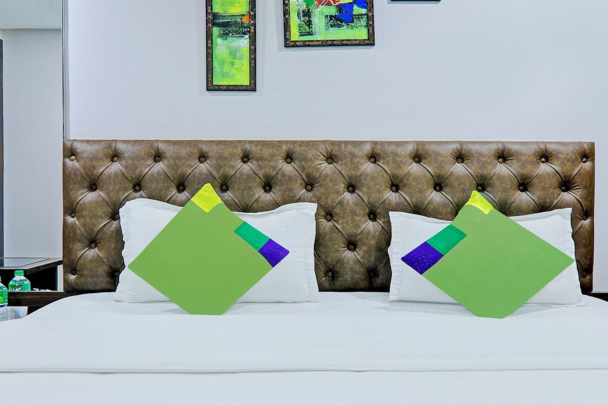 A hotel room with a tufted headboard, two pillows with geometric patterns, a white bedspread, and two framed artworks on the wall.