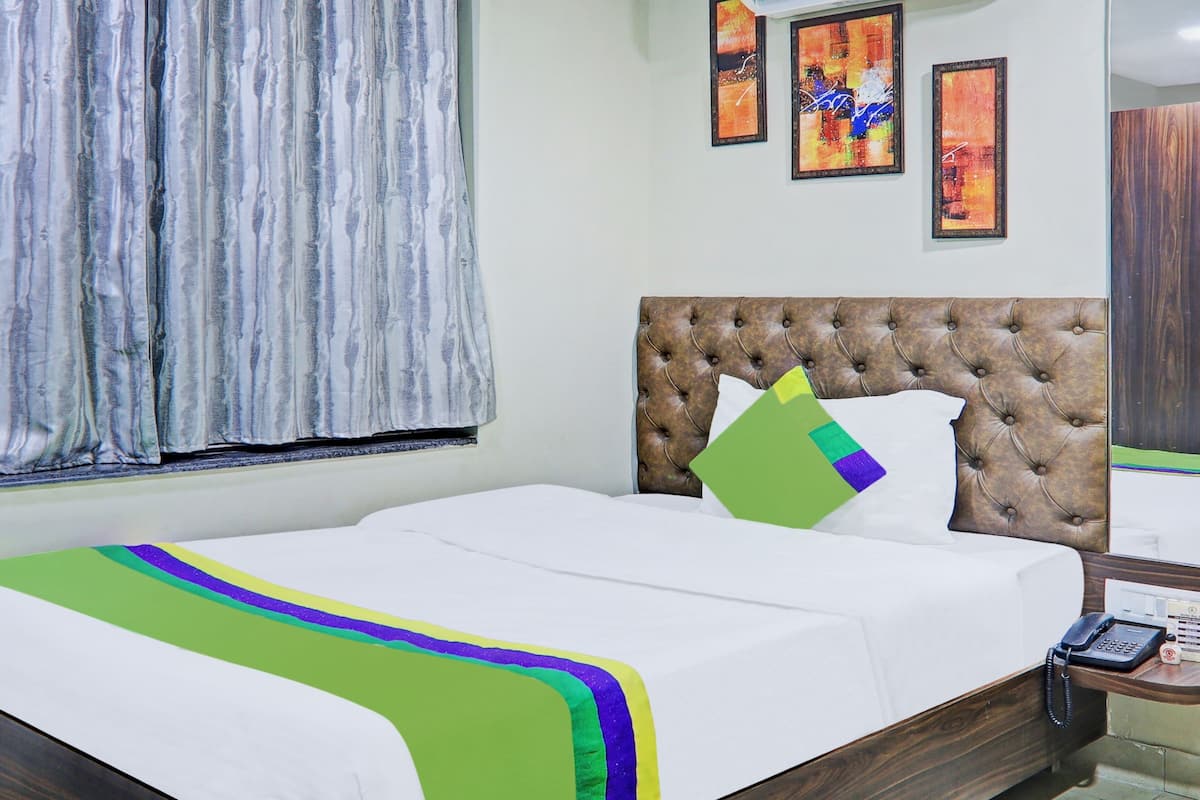 A hotel room with a bed, a telephone, and artwork on the wall.