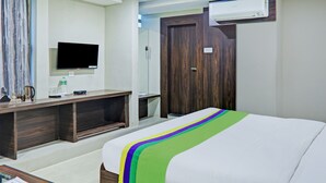 Una habitación de hotel con una cama, un televisor montado en la pared, un escritorio de madera y un armario.