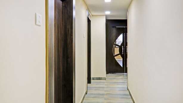 Un pasillo con una puerta de madera a la izquierda, una pared blanca y un piso de baldosas.