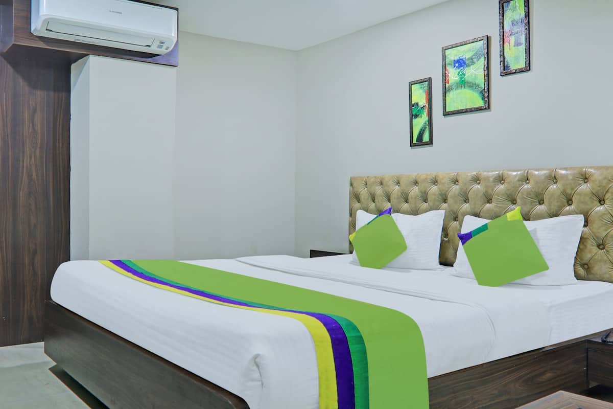 A hotel room with a bed, a bedside table, a telephone, and a wall-mounted air conditioner.