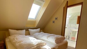 Een eenpersoonsbed in een kamer met een schuine hemel en dakraam, een klein nachtkastje en een deur naar een buitenruimte.
