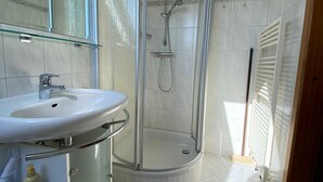 Een badkamer met een douche met glazen wand, een wit wastafelmeubel en een spiegel erboven.