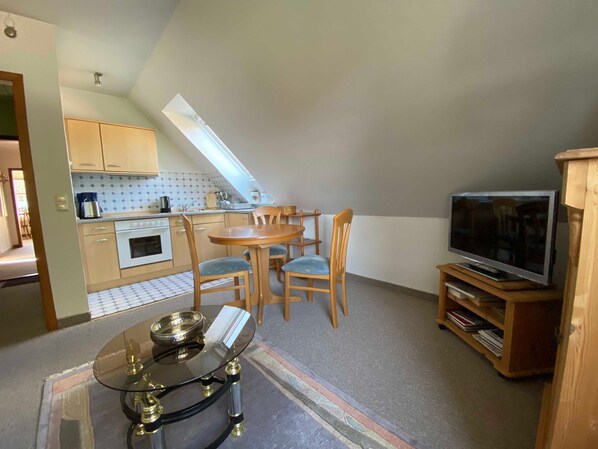 A compact kitchen with a dining area, a television, and a small table with a glass top.