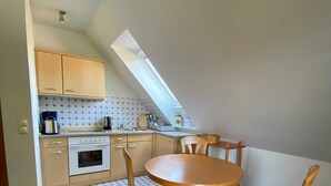 Een compacte keuken met een eethoek, met een tafeltje en stoelen, een inbouwoven en een dakraam.