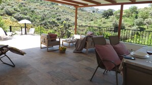 A covered outdoor seating area with two chairs, a table, and a view of a hilly landscape. - Casa rural rodeada de arboles frutales con piscinas privadas y wifi (Cómpeta)