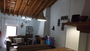 A living room with a wooden ceiling, a television, a sofa, and a dining table with placemats. - Casa rural rodeada de arboles frutales con piscinas privadas y wifi (Cómpeta)