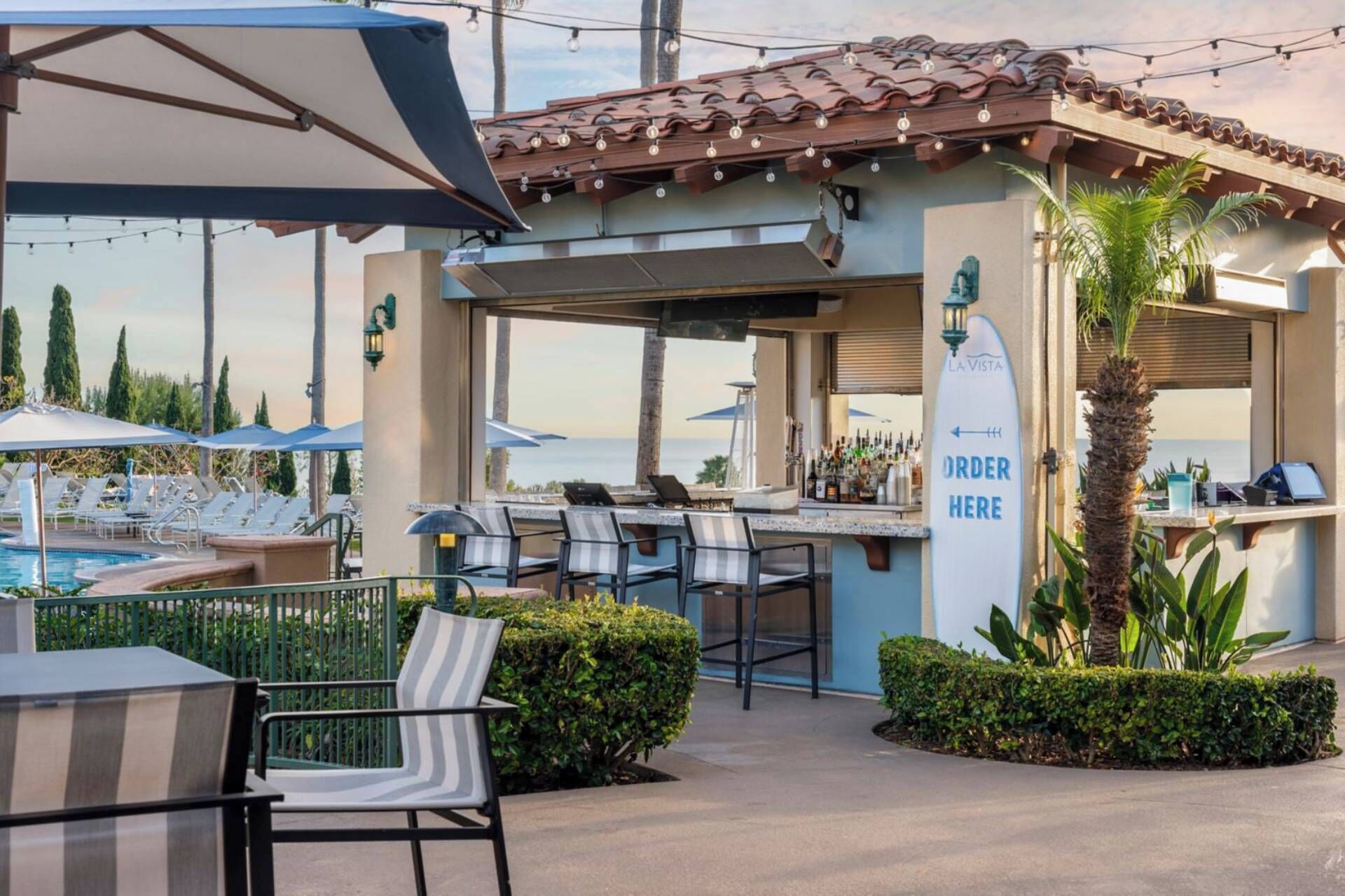 A poolside bar area with outdoor seating, a bar counter, and a sign indicating an order point.