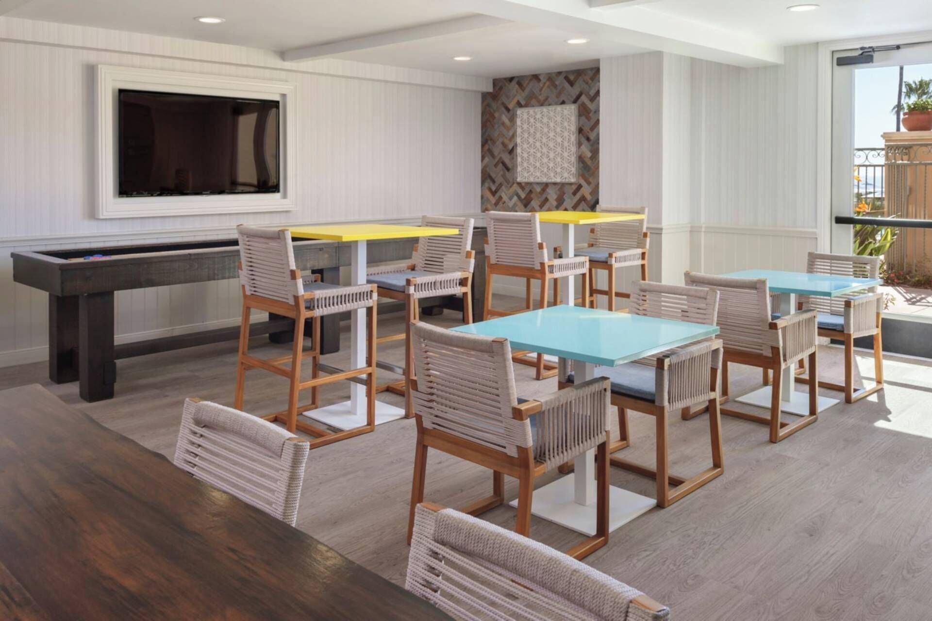 A dining area with wooden tables and chairs, a TV mounted on the wall, and a patterned wall decoration.