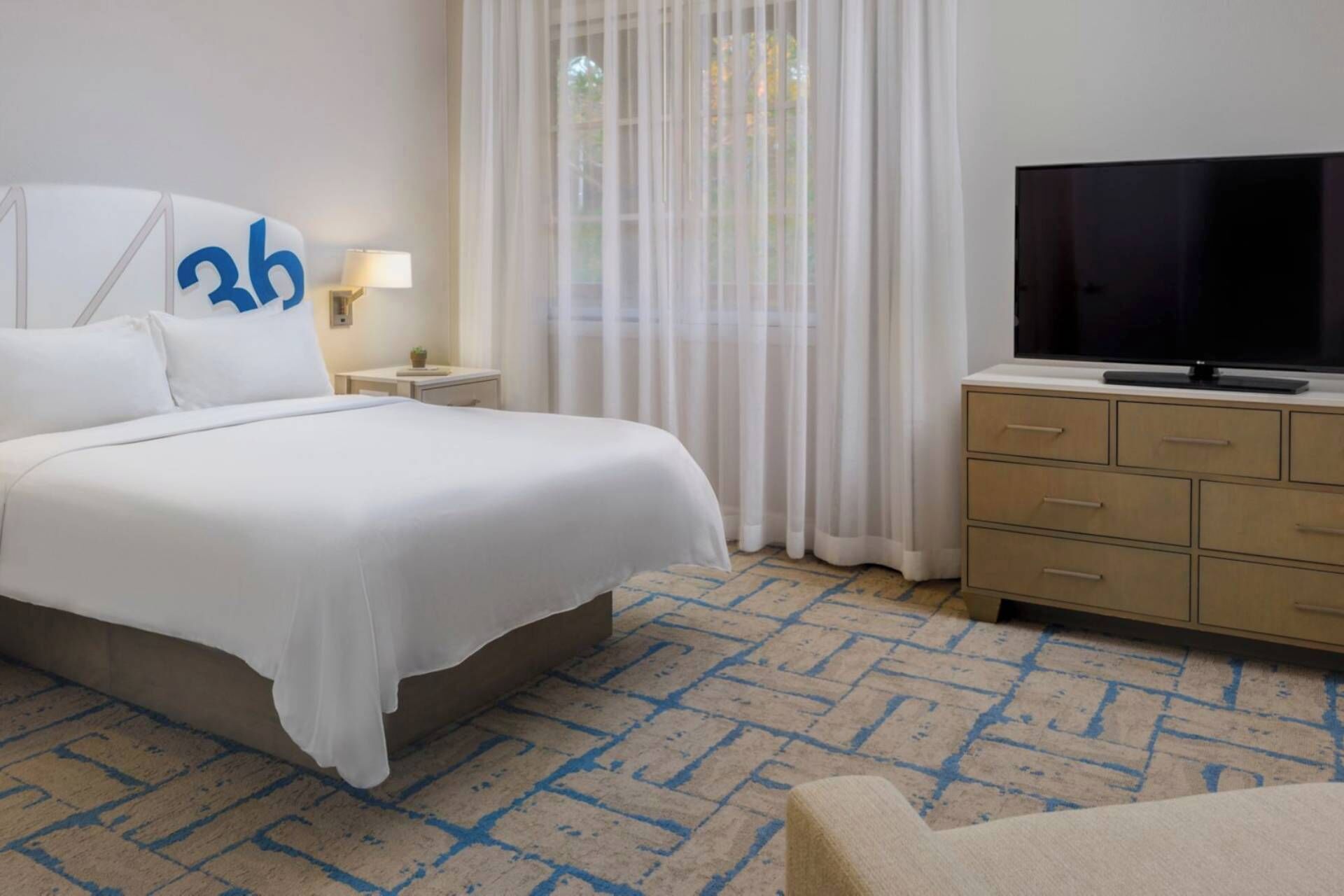 A hotel room with a bed, a TV, a nightstand, a lamp, and a dresser.