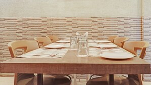 Una mesa de comedor dispuesta con platos, cubiertos y copas, flanqueada por sillas, frente a una pared con textura.