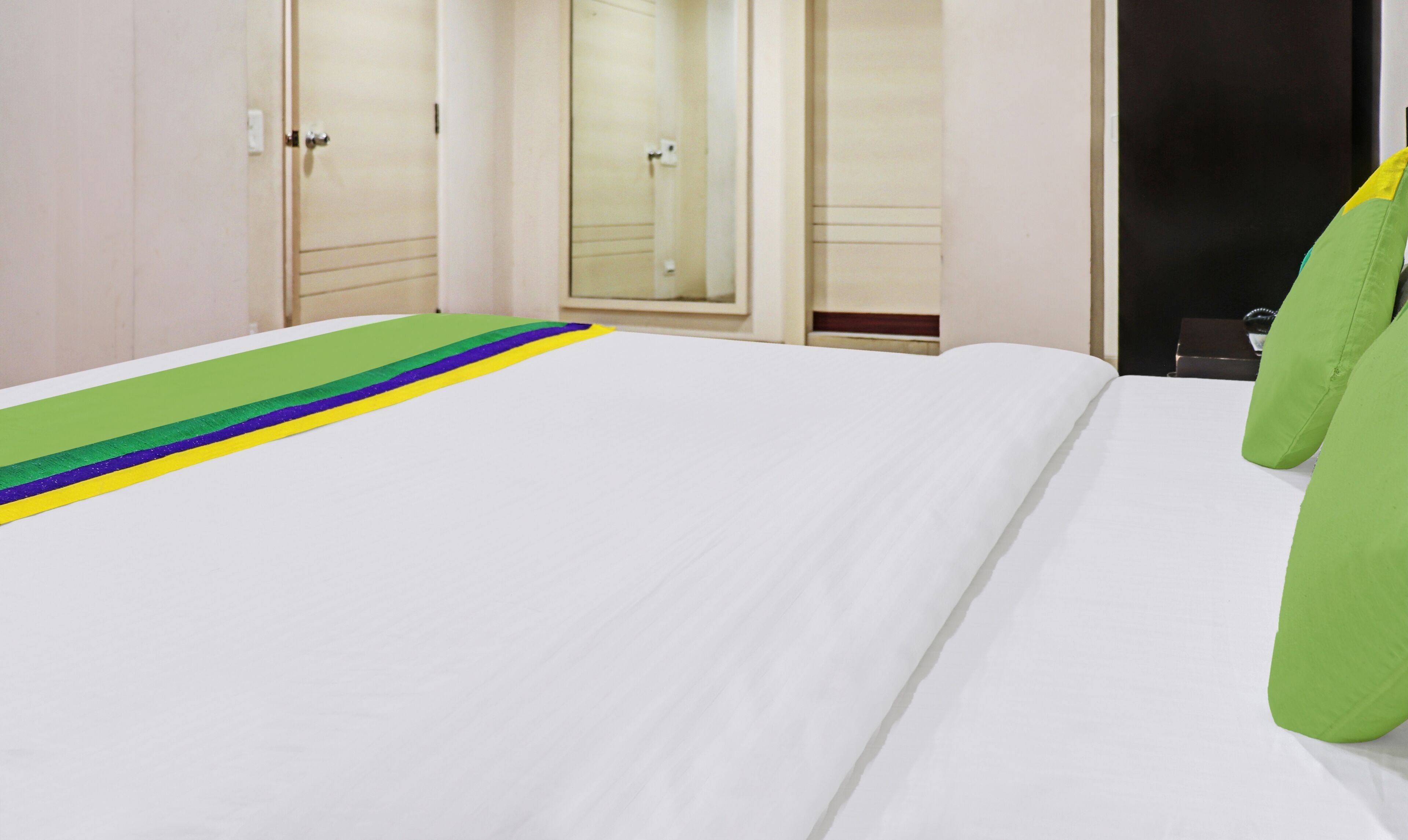 Una camera d'albergo con un letto rifatto, un cuscino verde e un tappeto a righe.