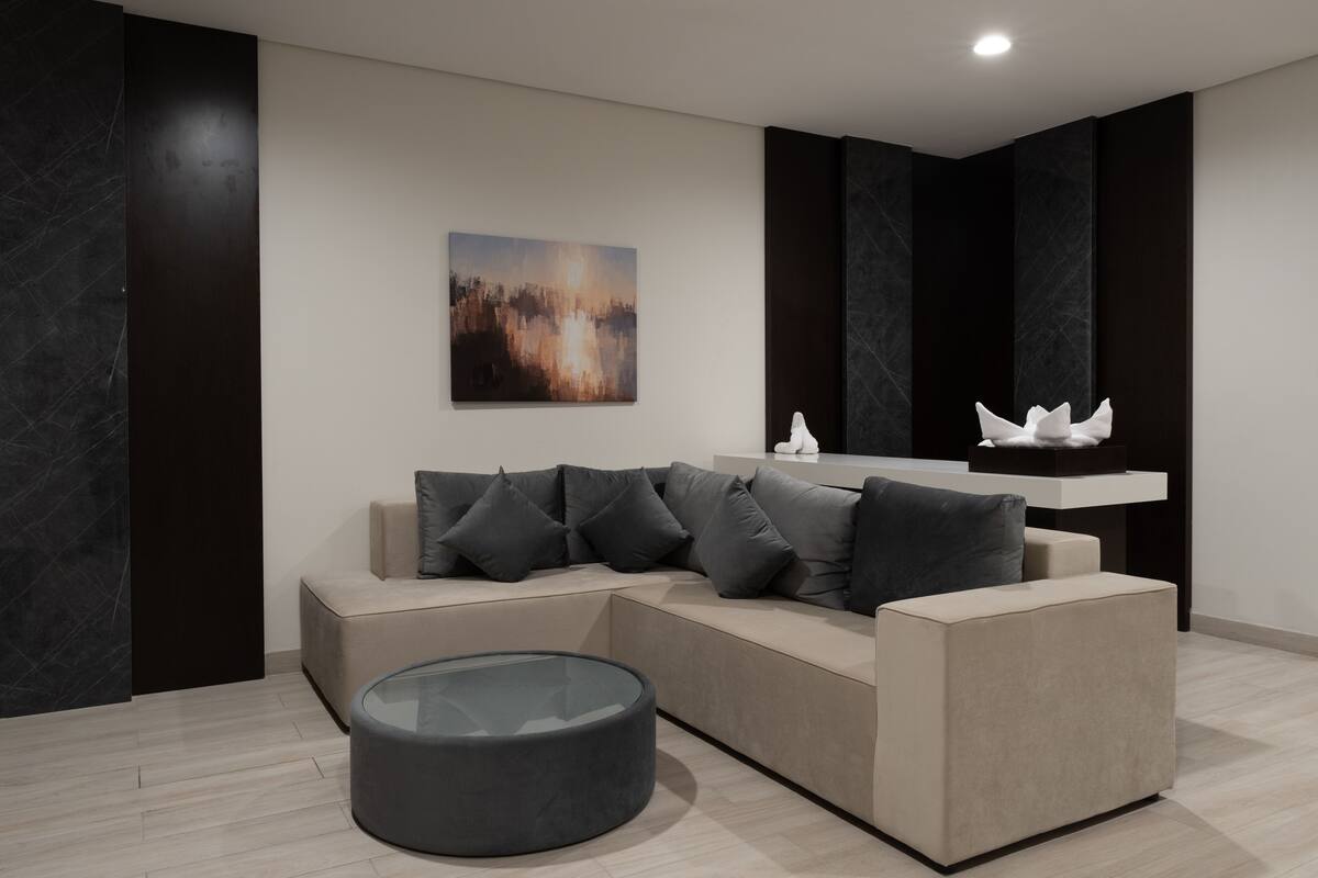 Un salon moderne avec un canapé d’angle, une table basse en verre et un tableau accroché au mur.