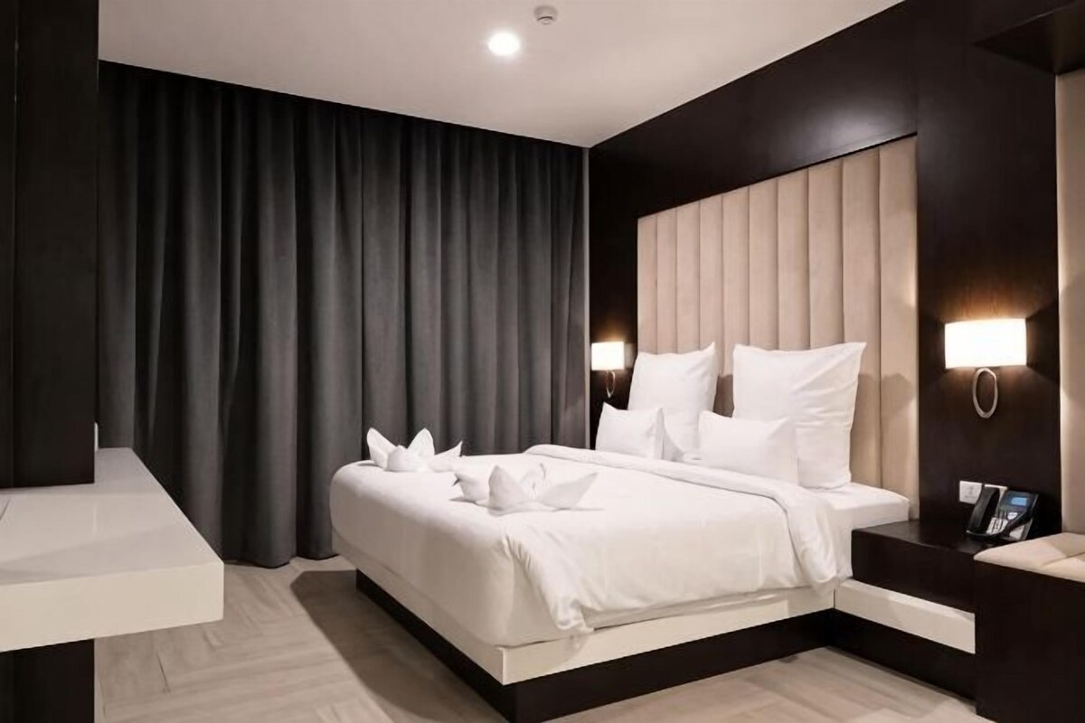 Una habitación de hotel moderna con una cama grande, una mesita de noche, un escritorio y una cortina oscura.
