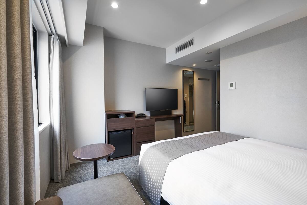 Une chambre d’hôtel équipée d’un lit, d’un bureau, d’une télévision et d’un petit réfrigérateur.