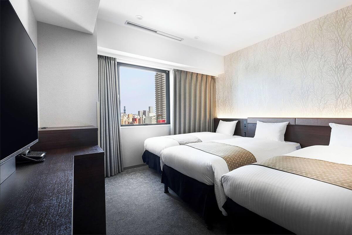 Une chambre d’hôtel avec deux lits, une grande fenêtre avec des rideaux, un téléviseur à écran plat et une vue sur la ville.