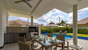 An outdoor patio with a dining table set for four, surrounded by wicker chairs. A grill and bar area is adjacent to the patio.