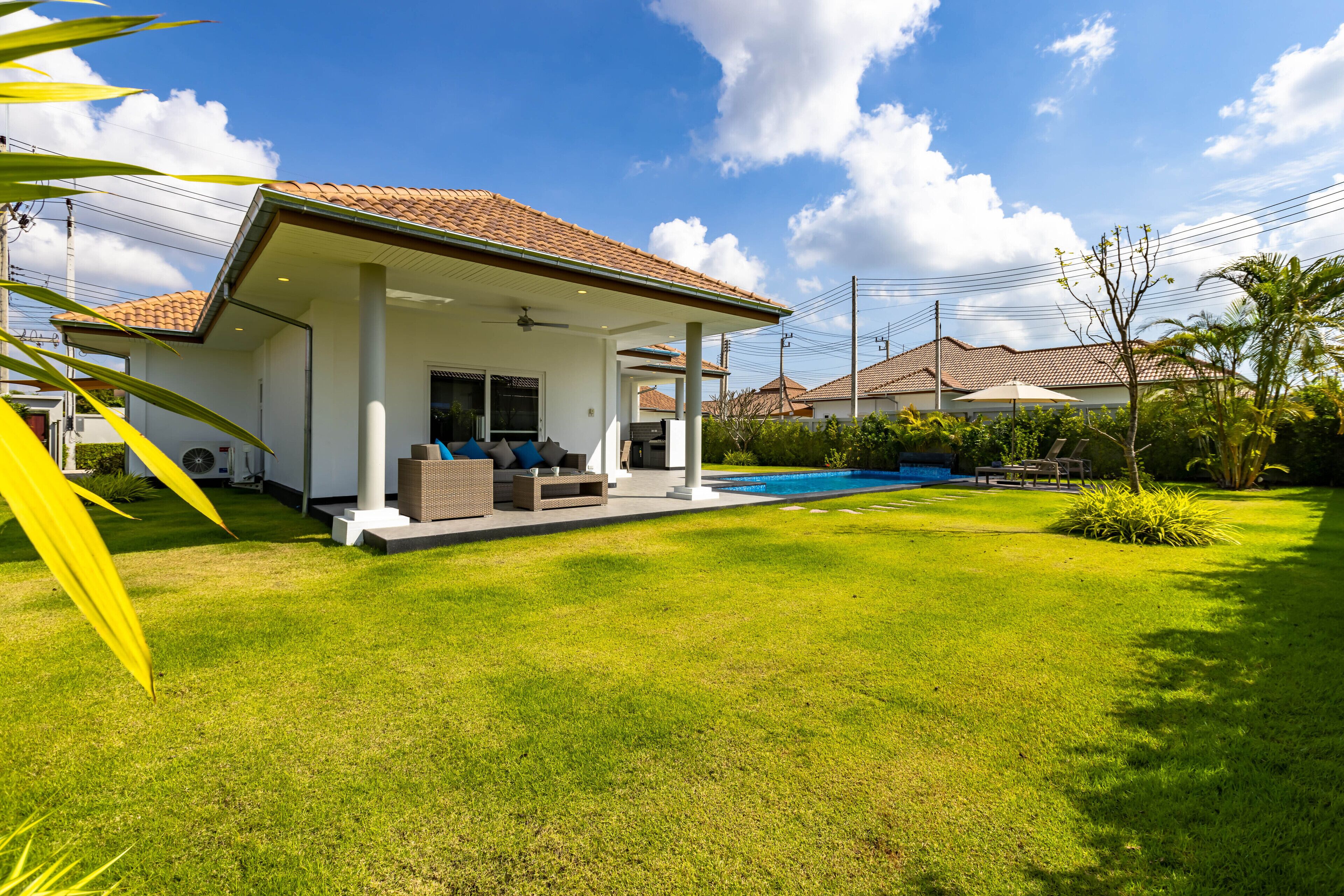 Uma casa com varanda coberta, piscina e gramado bem cuidado.