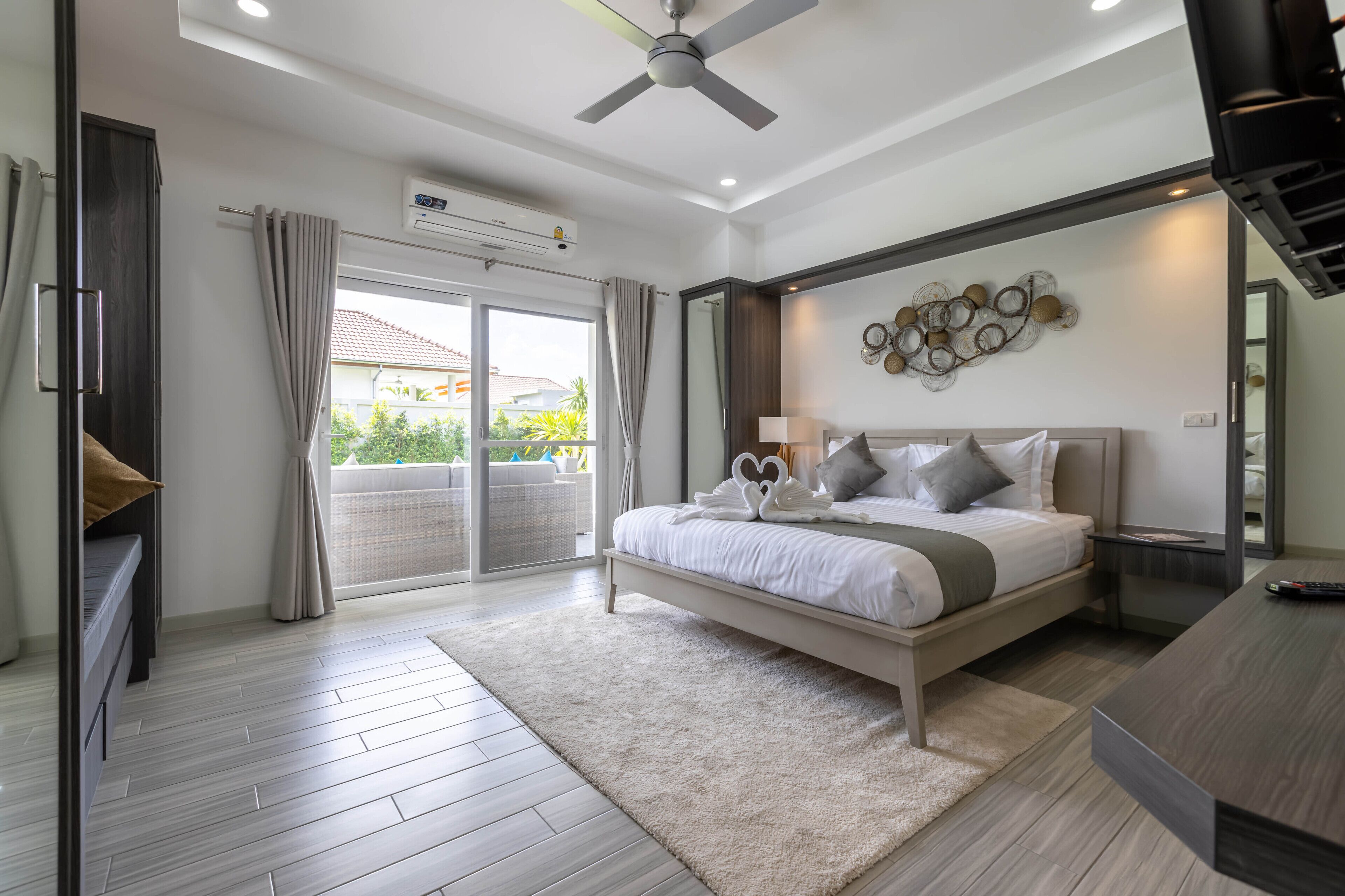 A modern bedroom with a large bed, a ceiling fan, a balcony with curtains, and a wall-mounted air conditioner.