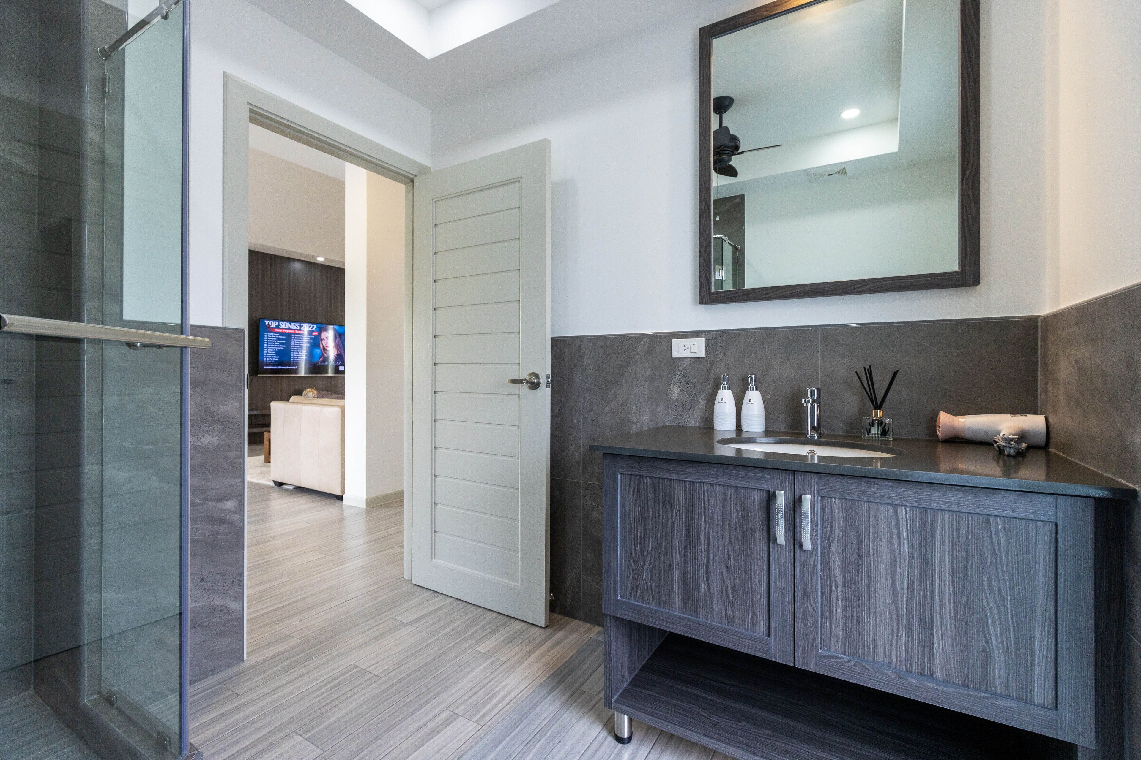 A modern bathroom with a dark wood vanity, a large mirror, and a glass shower enclosure.