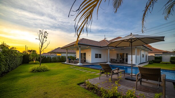 A modern house with a swimming pool, outdoor seating, and a well-maintained lawn.