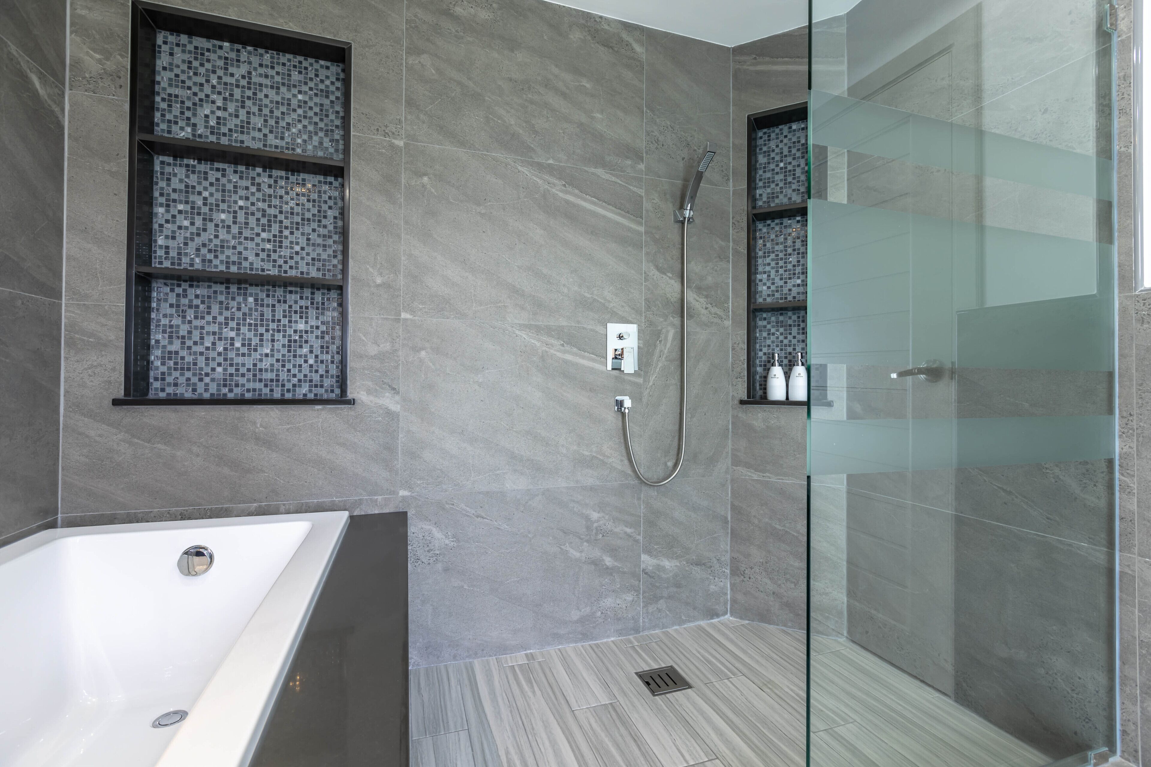 A modern bathroom with a glass shower enclosure, a bathtub, and a tiled shower area.
