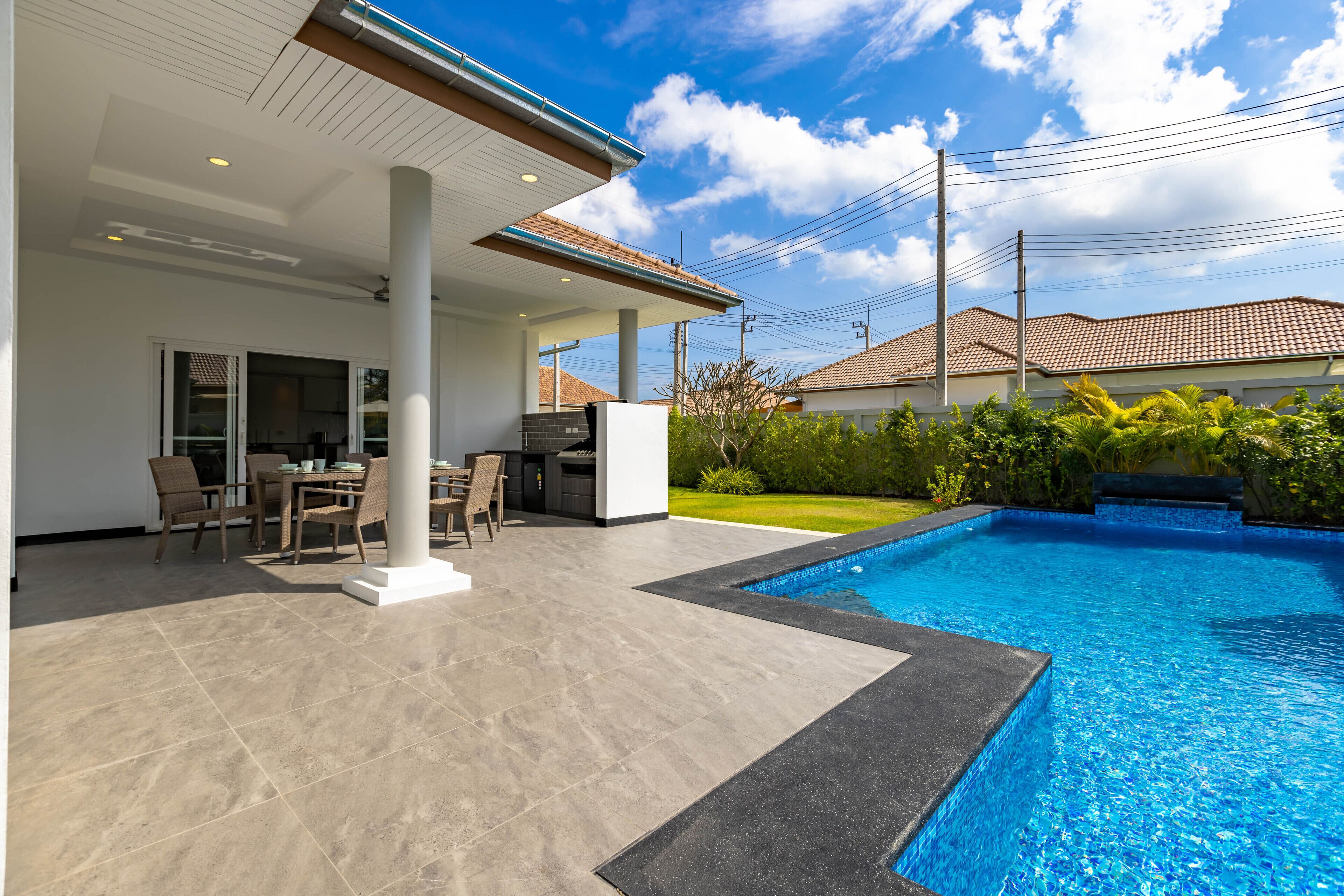 Un espace piscine extérieur moderne, doté d’un patio couvert, d’un ensemble de mobilier de jardin et d’une pelouse bien entretenue.