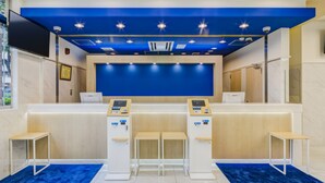 Uma área de recepção com parede azul, dois caixas eletrônicos e um balcão.