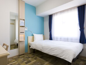 A hotel room with a bed, a bedside table, a mirror, a wall-mounted control panel, and a window with curtains.