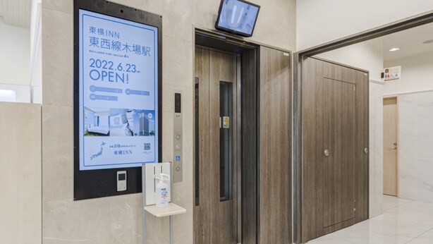 Área de recepção de hotel com painel digital exibindo a data de abertura e comodidades.