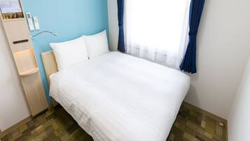 Ein Hotelzimmer mit einem Bett, einem Nachttisch aus Holz, einer kleinen Ablage und einem Fenster mit Vorhängen.