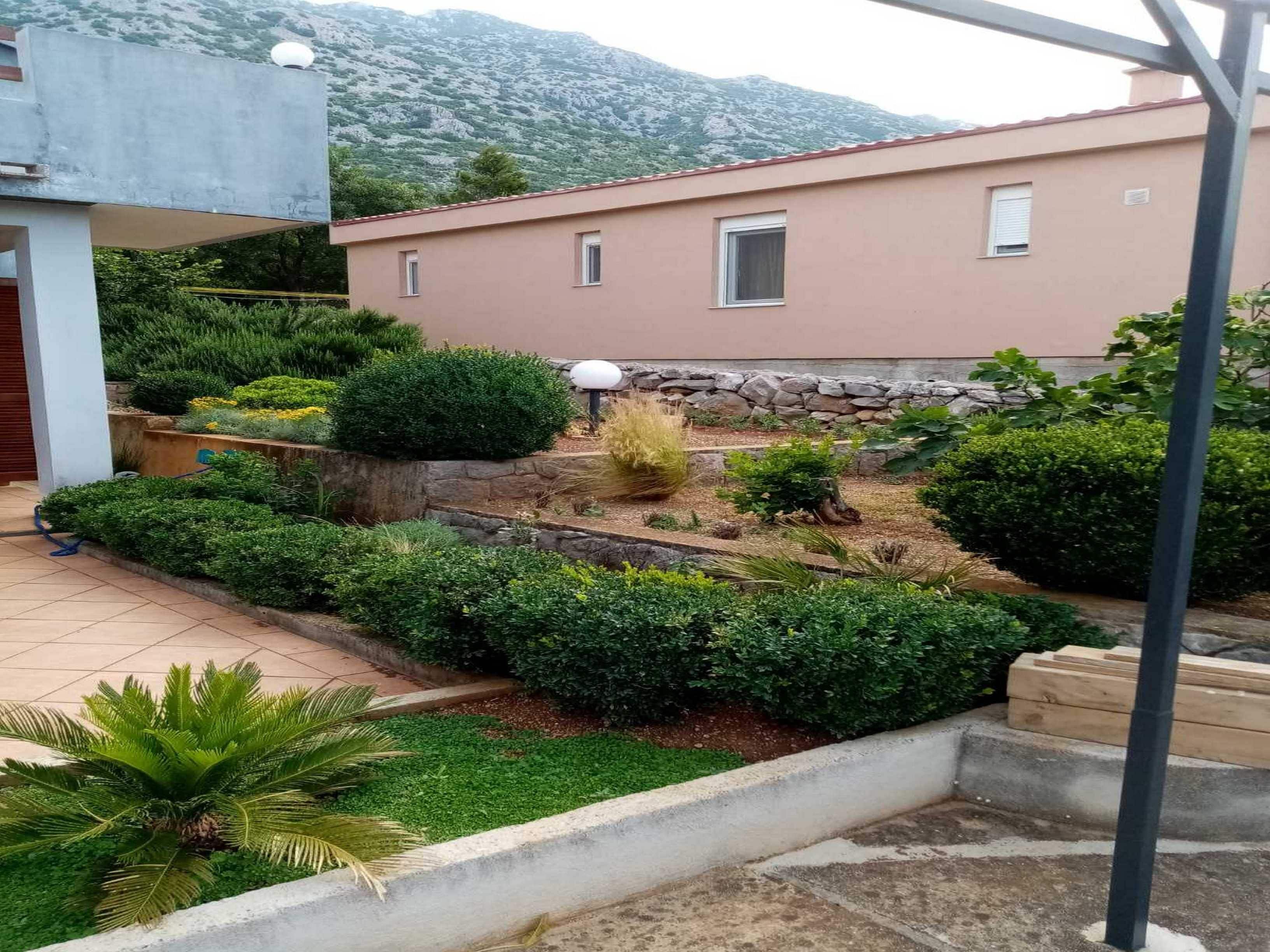 A residential area with a well-maintained garden, a stone wall, and a building with a flat roof.