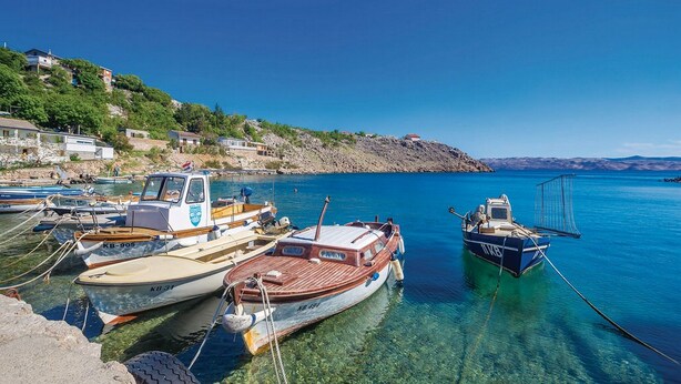 A marina with several boats docked, clear blue water, and a hillside with buildings. - Apartments Paola (Karlobag)