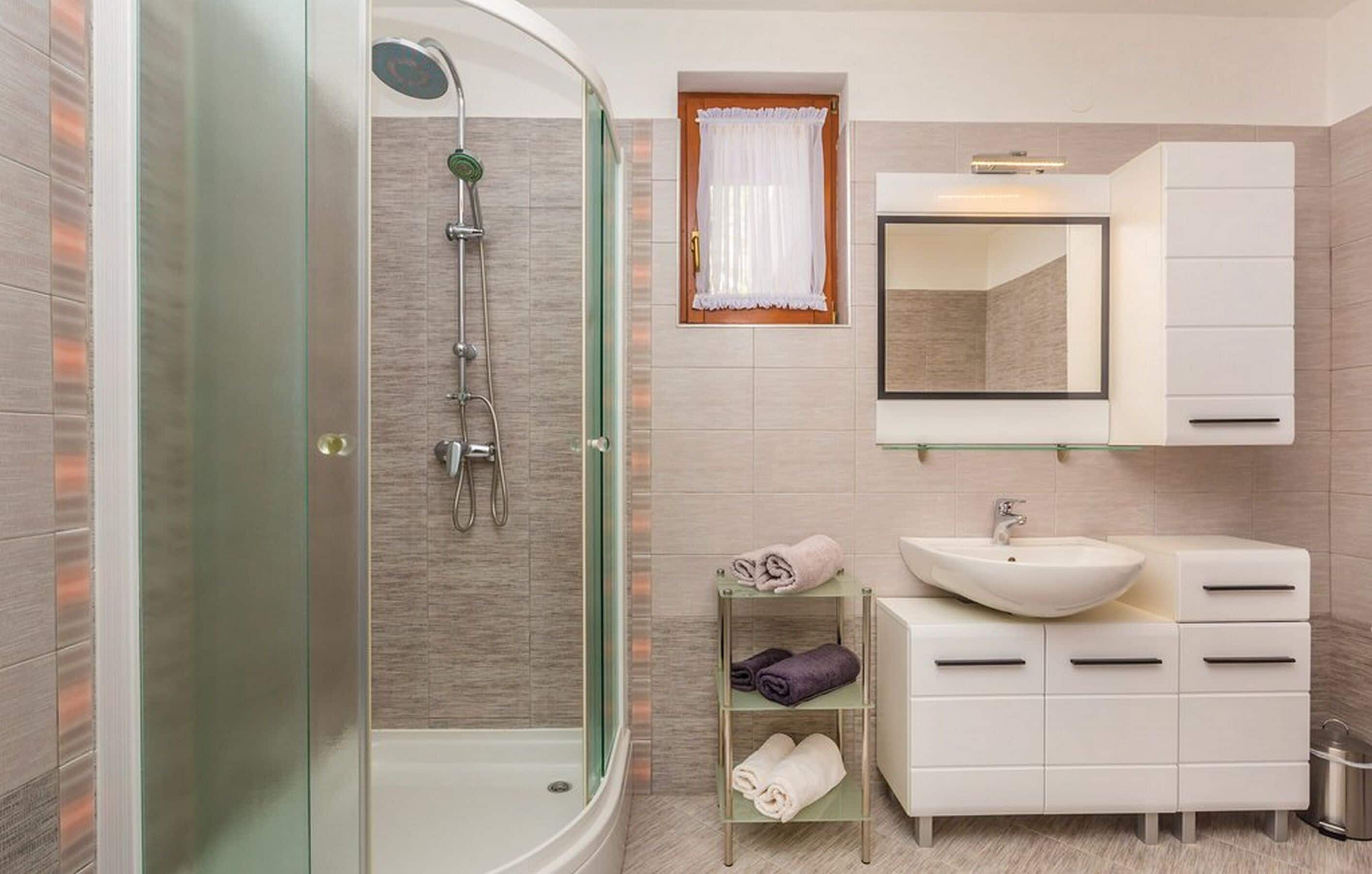 Un baño moderno con ducha de vidrio, lavamanos blanco y tocador con cajones.