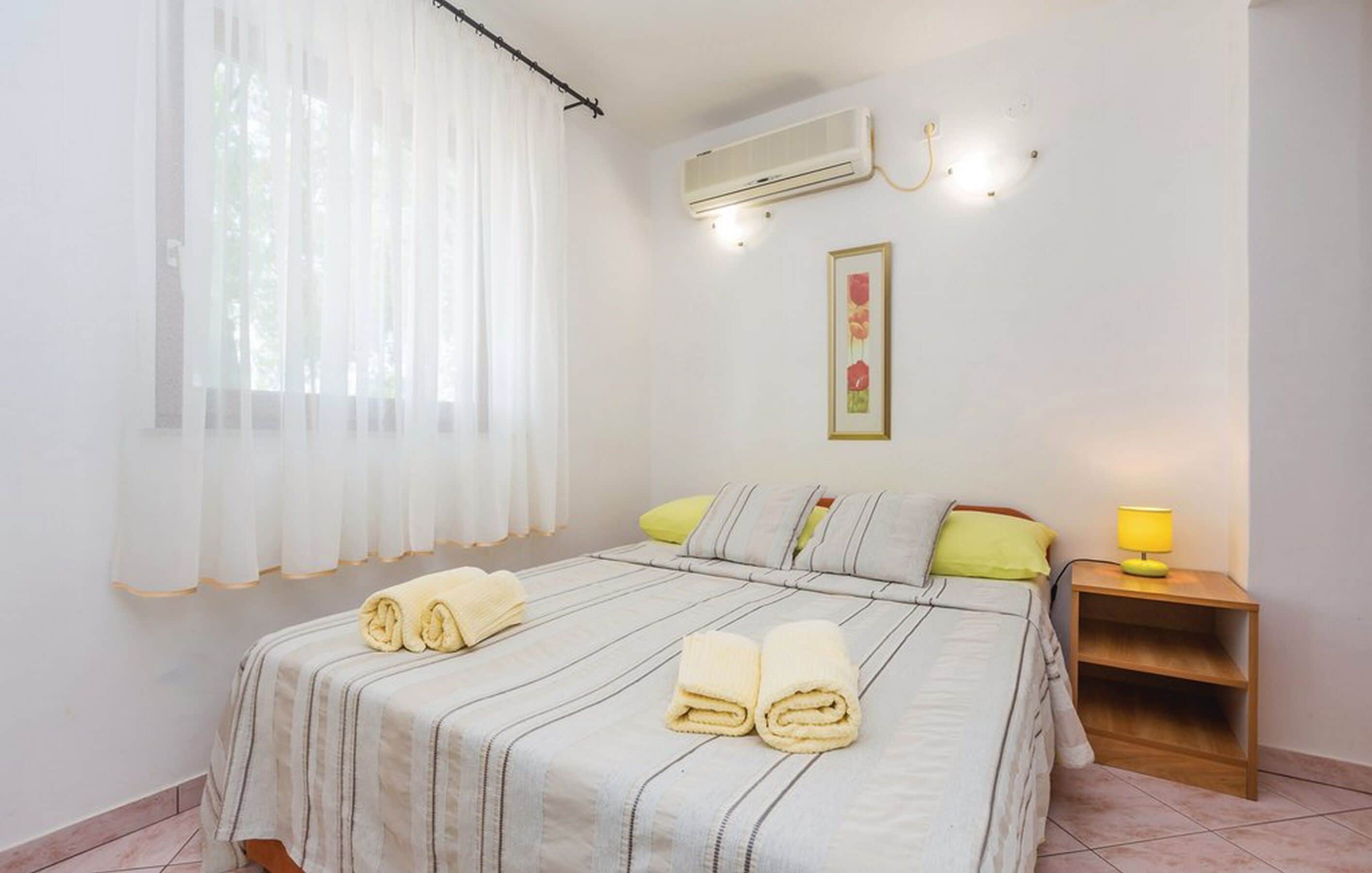Ein Schlafzimmer mit Bett, Nachttisch, Klimaanlage, einem Fenster mit Vorhängen und einer Wandleuchte.