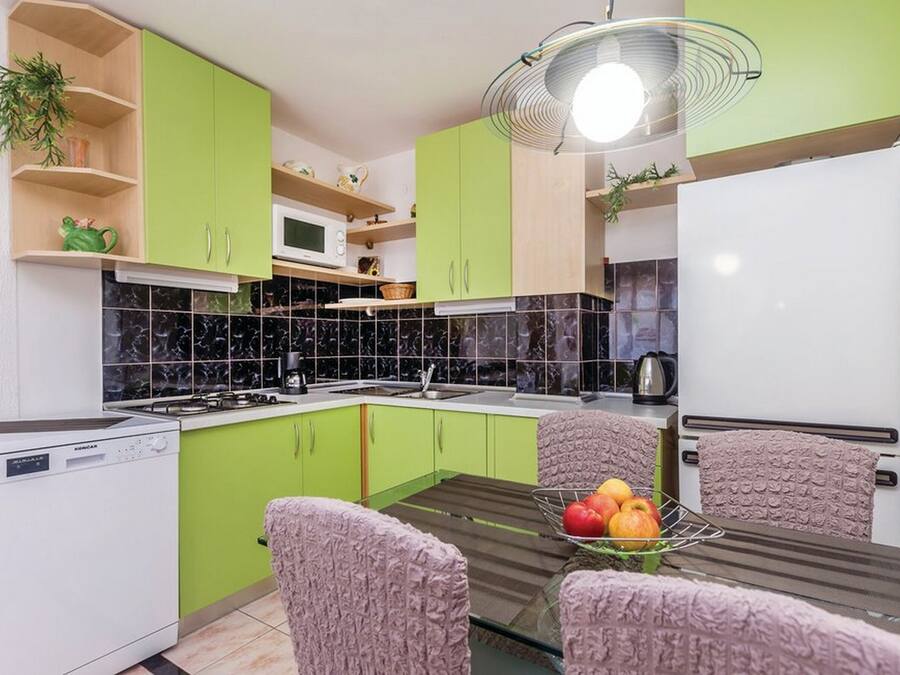 A compact kitchen with green cabinets, a microwave, a stove, and a dining area with a table and chairs.
