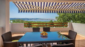 A balcony with a table and chairs, a striped awning, and a view of a landscape. - Apartments Paola (Karlobag)