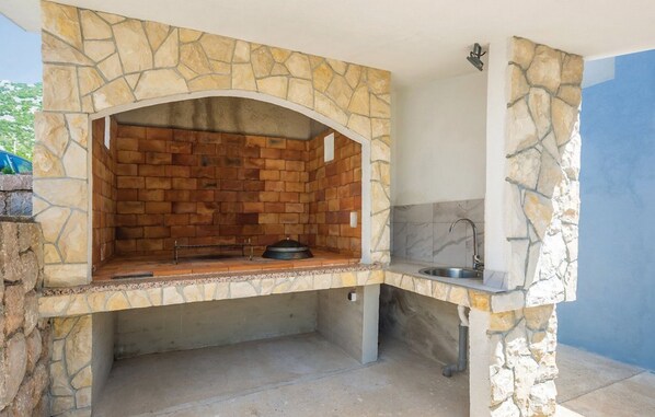 Una cocina exterior con estructura de arco de piedra, un lavamanos y una parrilla.