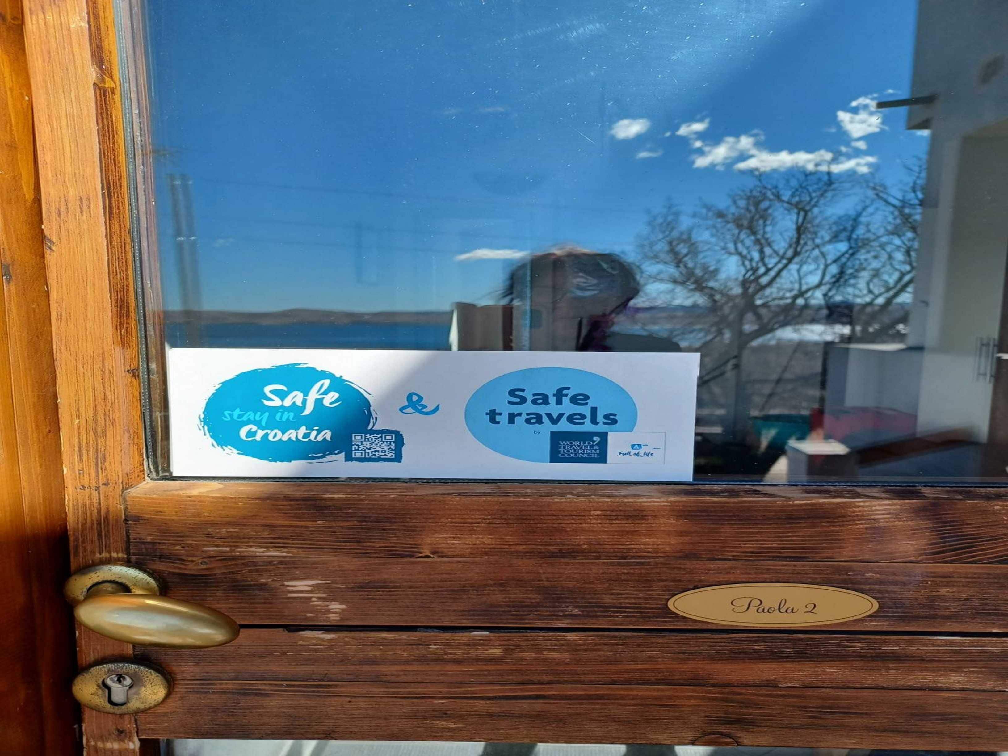 Una puerta de madera con un cartel que indica 'Safe travels by World Tourism Council' y una placa con el nombre 'Paola 2'.