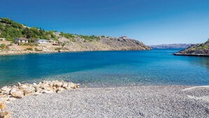 A coastal area with a pebble beach, clear blue water, and buildings on a hillside. - Apartments Paola (Karlobag)