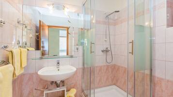 A modern bathroom with a glass shower enclosure, a white sink, and a glass-topped vanity.
