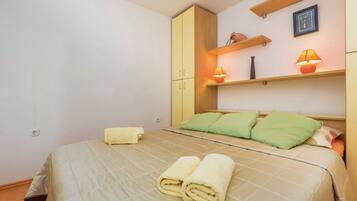 A bedroom with a bed, green pillows, a yellow towel, and a wooden wardrobe.