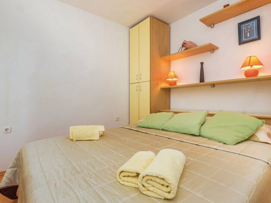 A bedroom with a bed, green pillows, a yellow towel, and a wooden wardrobe.