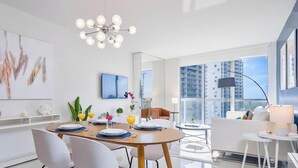 A modern living room with a dining area, large windows, and a city view.