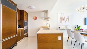 A modern kitchen with wooden cabinets, a central island, and a dining area with white chairs.