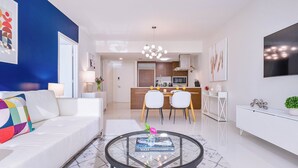 A modern living room with a white sofa, a glass coffee table, and a dining area with two chairs.
