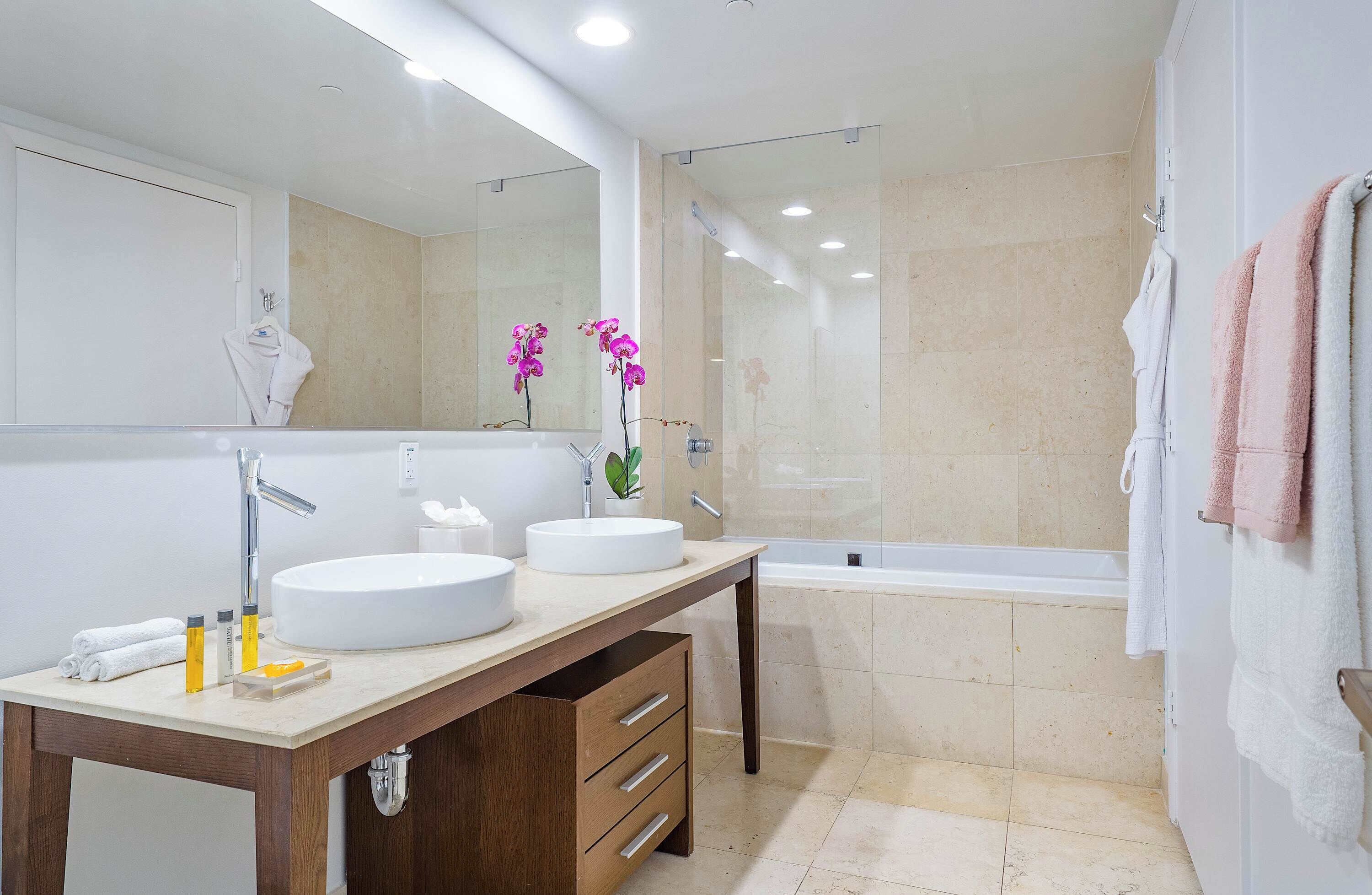 A modern bathroom with a large mirror, two sinks, a vanity, and a bathtub.