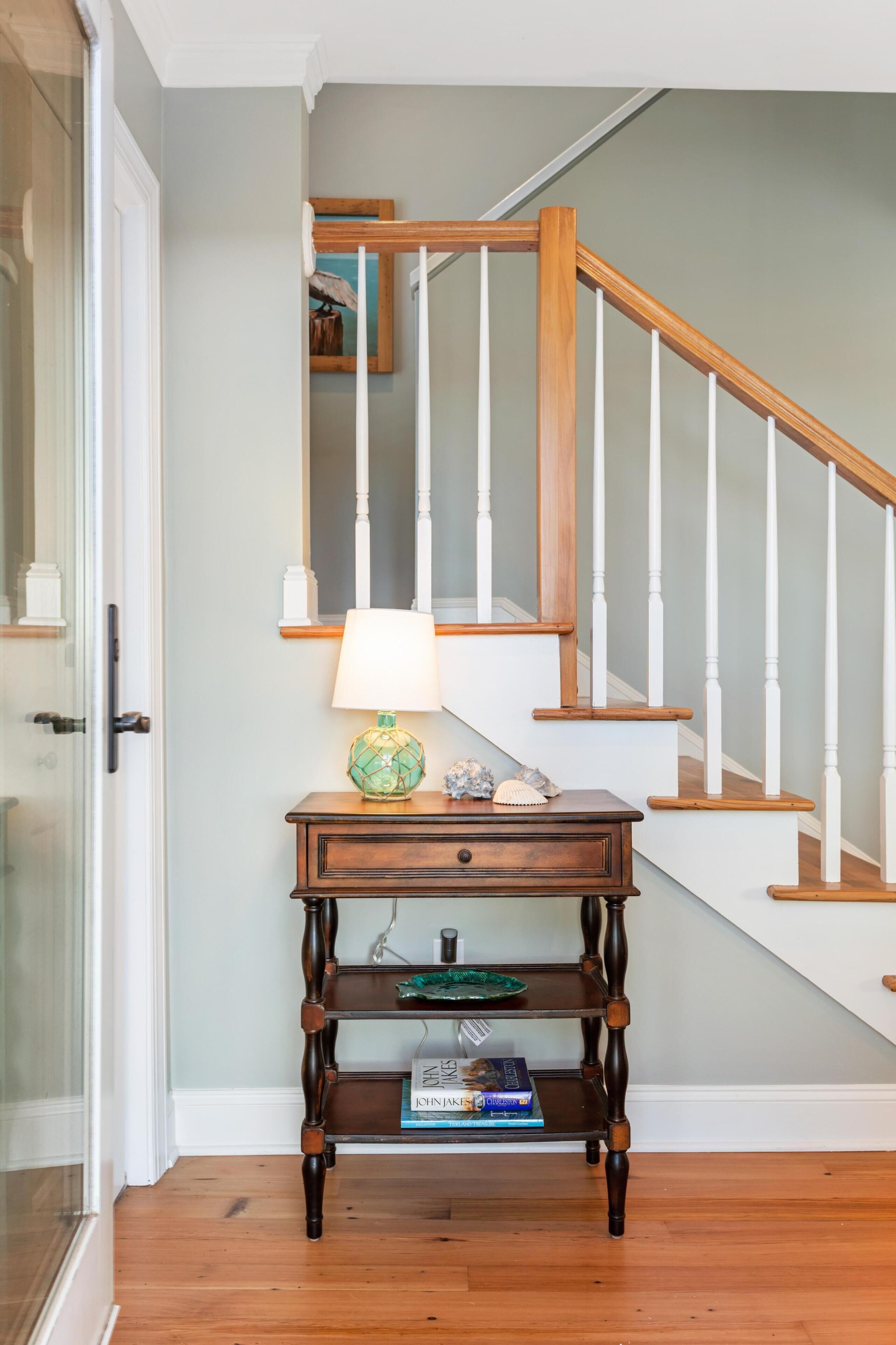 Een trap met houten treden en witte balustrades, een klein houten tafeltje met een lamp en decoratieve objecten, en een glazen deur aan de linkerkant.